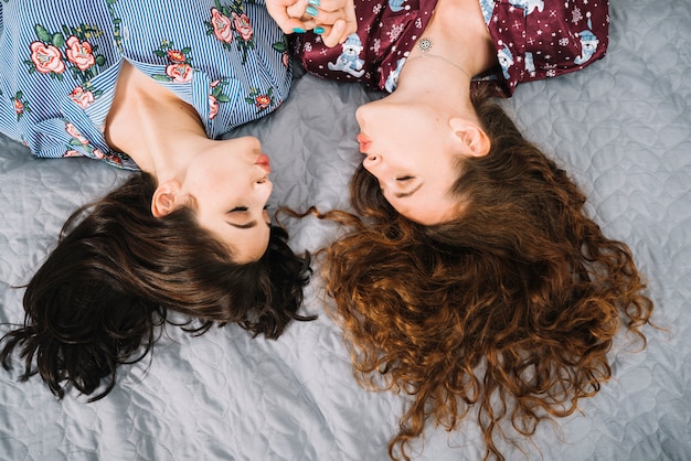 Накладные зрения двух женщин-друзей, надувая губы, лежа на кровати