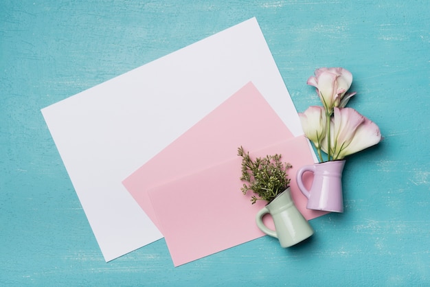 An overhead view of two flower vases with blank pink and white paper on textured background