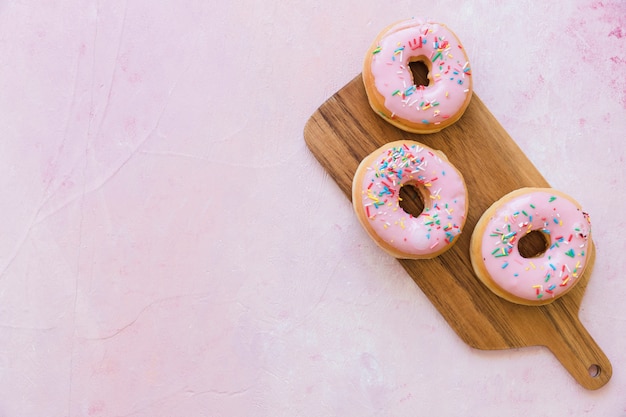 Overhead view of two fresh pink donuts on wooden chopping board