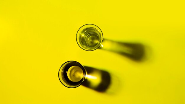 An overhead view of two glasses of pure water with shadow falling on yellow background