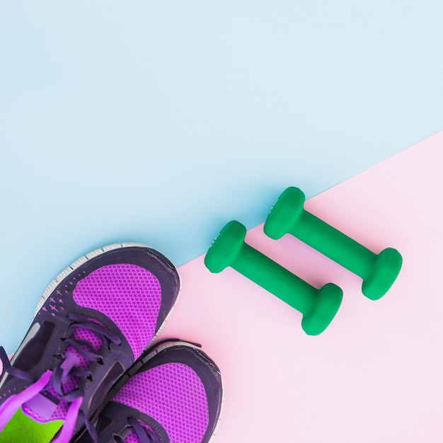An overhead view of two green dumbbells and pair of shoes on dual background