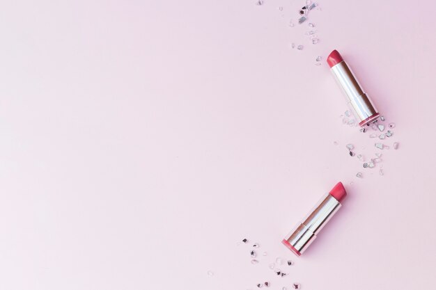 Overhead view of two pink lipsticks and crushed glass pieces on pink background