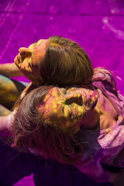 An overhead view of two women sitting back to back with holi color on their face