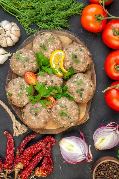 Overhead view of uncooked meatballs on a wooden cutting board and fresh vegetables green on dark wave background