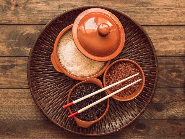 Overhead view of uncooked organic rice grains bowls on wooden tray with chopstick