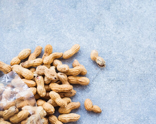 An overhead view of unpeeled peanuts on rough textured background