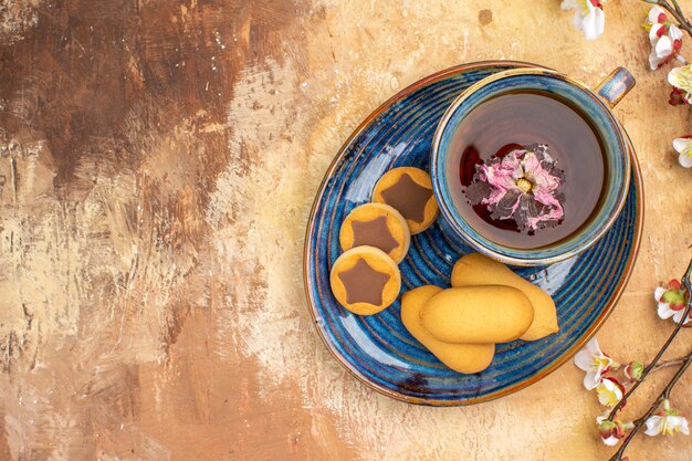 Overhead view of various biscuits a cup of tea and flowers on mixed color table