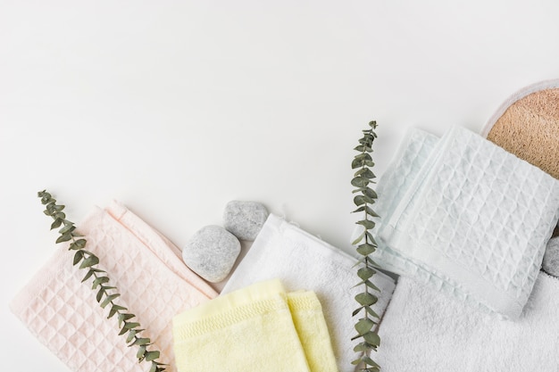 An overhead view of various folded napkins with spa stones and twigs on white background