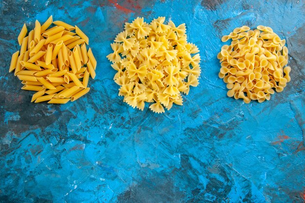 Overhead view of various raw Italian pastas arranged in a row on blue background