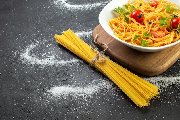 Free photo overhead view of vegan spagetti meal with tomatoes and green on a square shaped plate raw pastas tied up by a rope