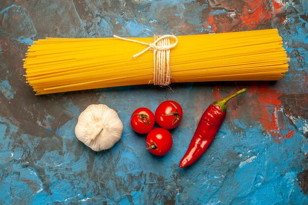 Overhead view of vermicelli pastas tied with rope and tomatoes pepper garlic on blue background