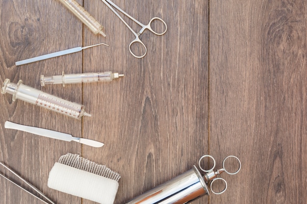 An overhead view of vintage stainless steel syringe; otoscope and medical equipment's on wooden desk