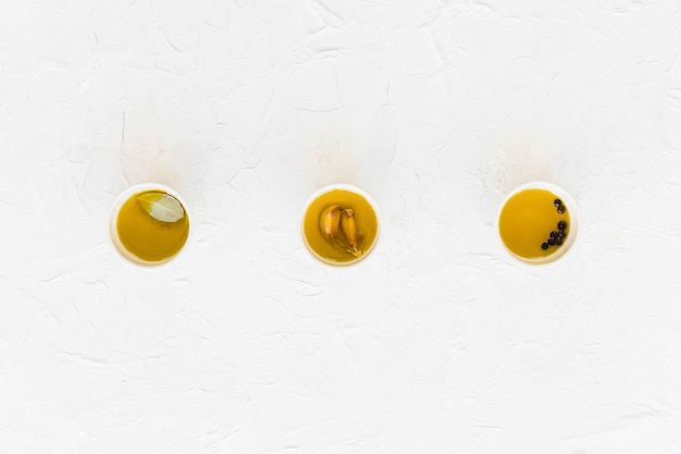 Overhead view of vivid garlic, black pepper and olive oil on white backdrop