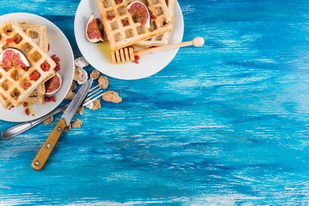 An overhead view of waffles with fig slices on plate against wooden blue textured background
