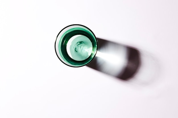 An overhead view of water in green glass on white backdrop