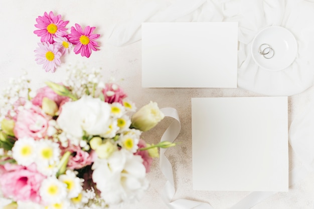 Вид сверху на свадебные букеты с белой карточкой и кольцами на бетонном фоне