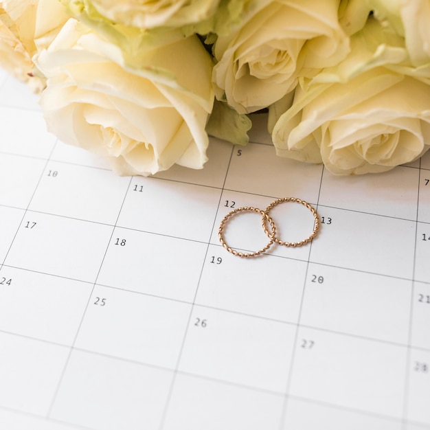 An overhead view of wedding rings and roses on calendar