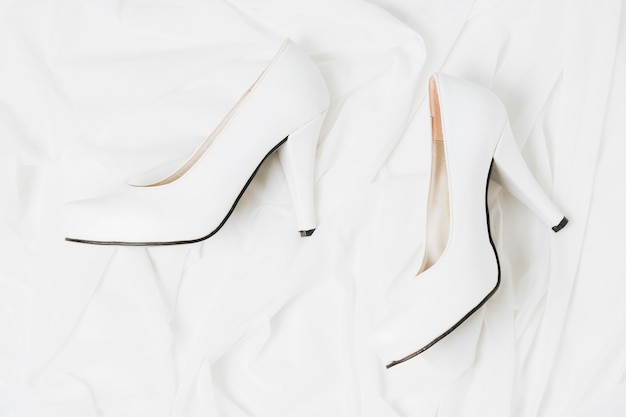 An overhead view of wedding white high heels on white cloth