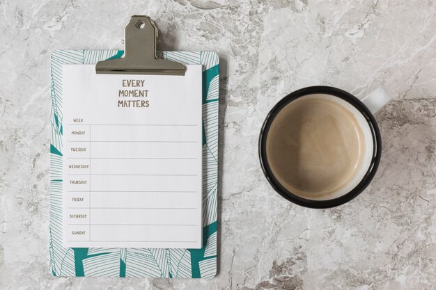 an overhead view of weekly plan on clipboard and cup of coffee