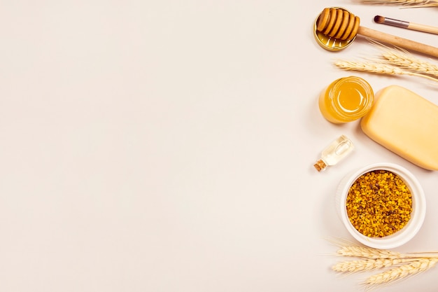 Overhead view of wheat ears; bee pollen; essential oil; soap; honey; honey dipper and makeup brush