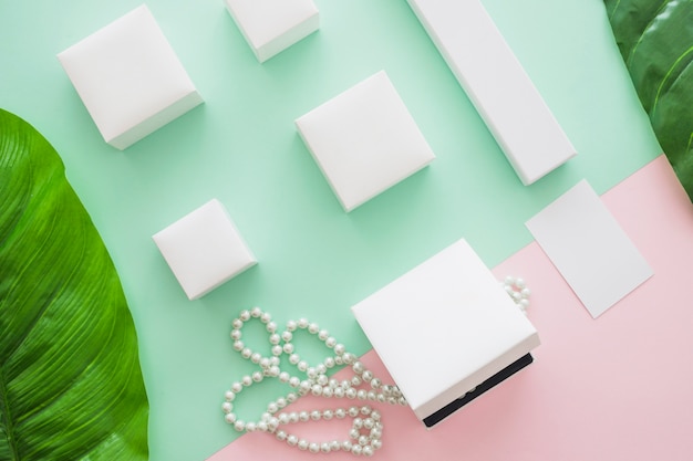 Overhead view of white boxes with pearls and leaf on colored background