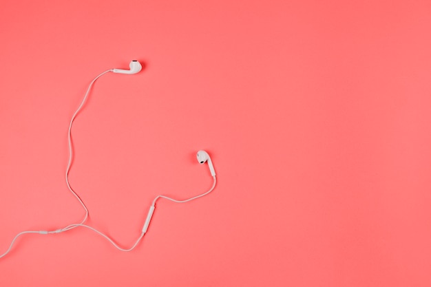 Free photo an overhead view of white earphones on coral background