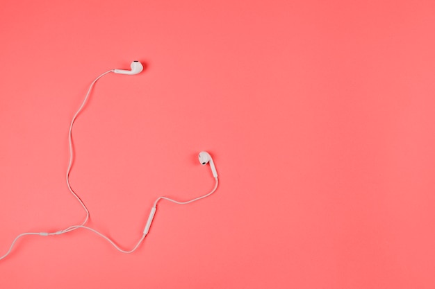 An overhead view of white earphones on coral background