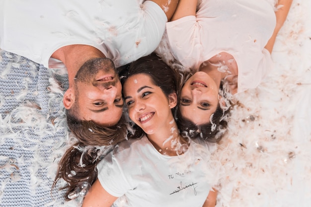 An overhead view of white feather over friends lying on bed