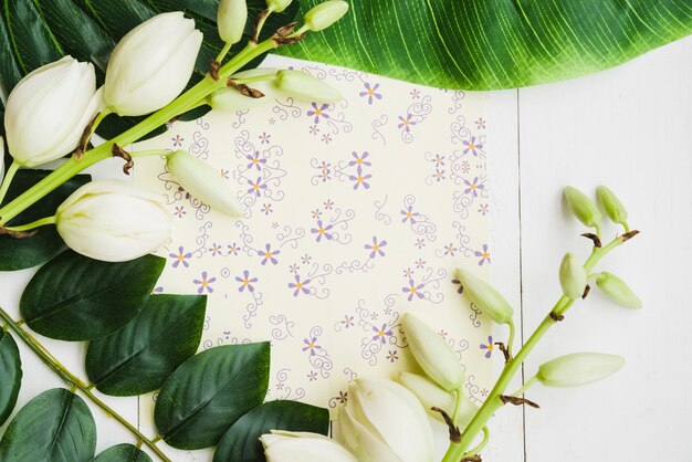 An overhead view of white flower twig on floral paper over the wooden backdrop