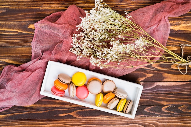 Free photo an overhead view of white gypsophila and macaroons in white box over the wooden table