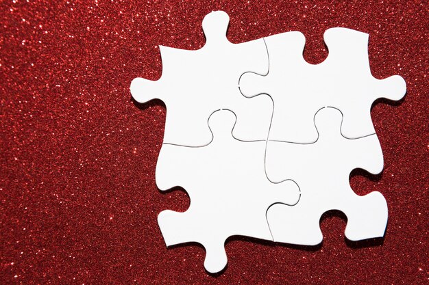 Overhead view of white jigsaw puzzle on red glitter background