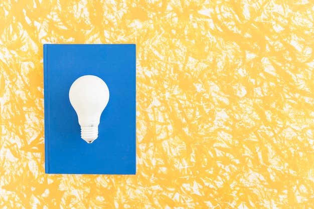 Overhead view of white light bulb on blue notebook over the pattern background