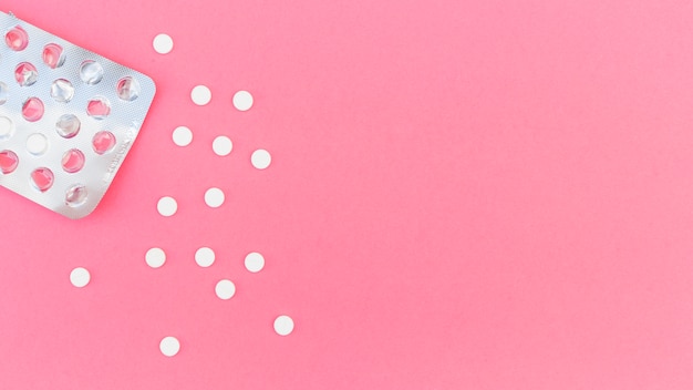 An overhead view of white round pills out from blister pack on pink background