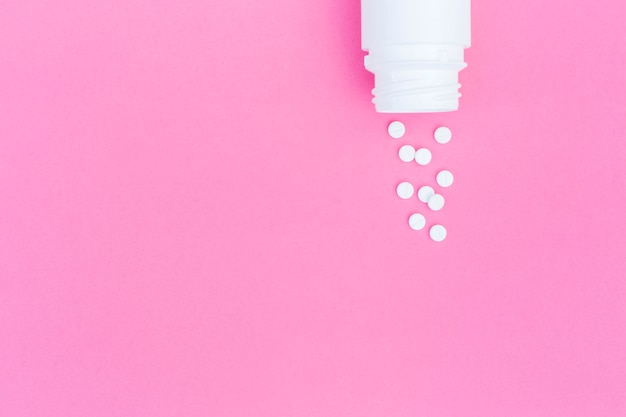 Una vista aerea delle pillole rotonde bianche versato dalla bottiglia su sfondo rosa