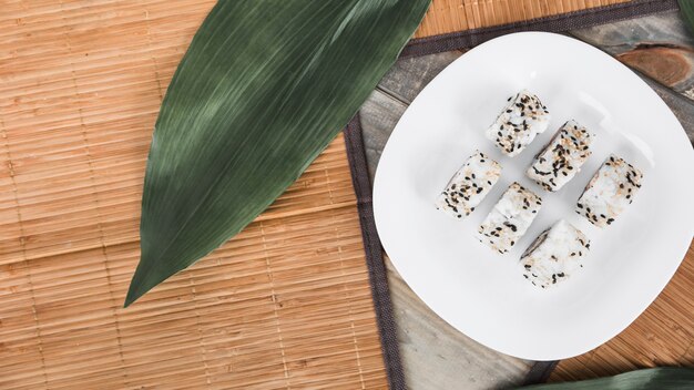 An overhead view of white sushi roll in plate with green leaves and placemat