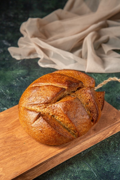 Overhead view of whole fresh black bread on brown wooden cutting board on dark colors surface