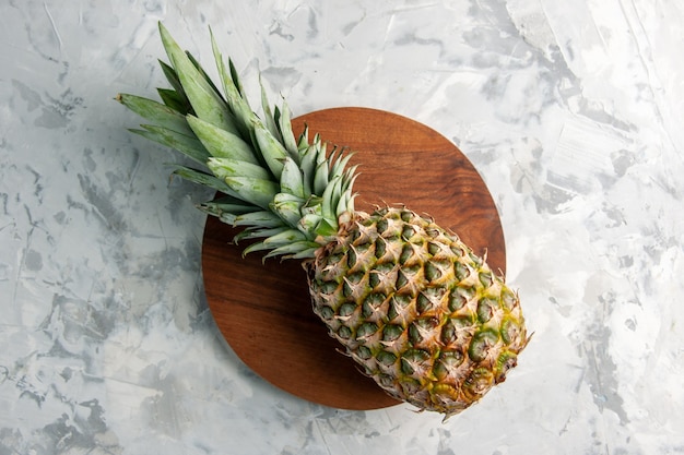 Overhead view of whole fresh golden pineapple on cutting board on marble surface