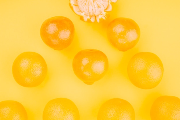 An overhead view of whole oranges on yellow backdrop