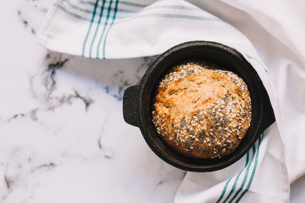 Free photo an overhead view of wholegrain loaf of bread in black container on marble top