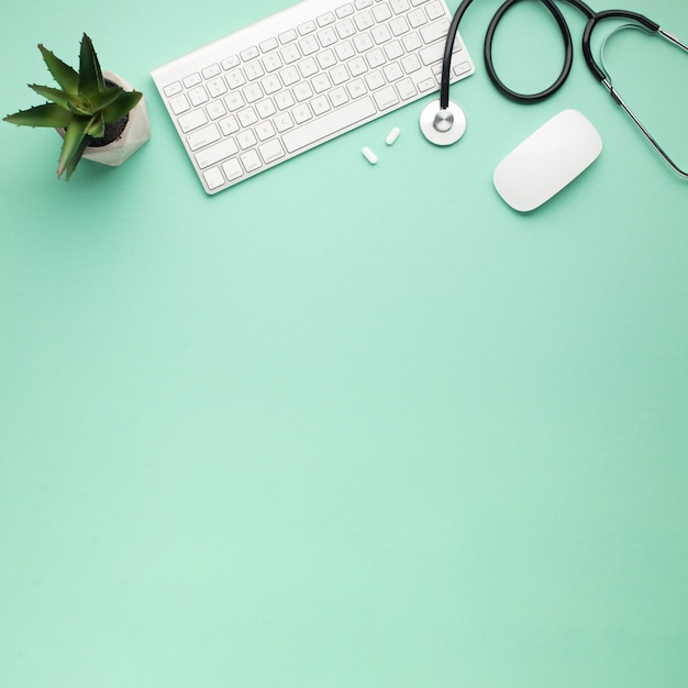 Overhead view of wireless keyboard and mouse near stethoscope with pills and succulent plant