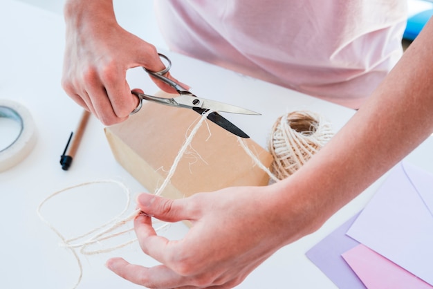 An overhead view of a woman cutting the jute thread with scissor on table