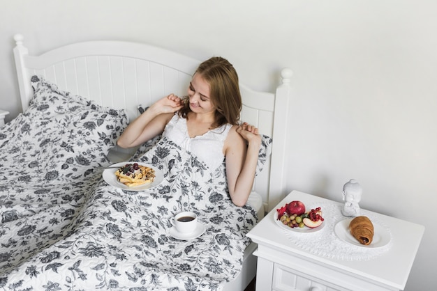 An overhead view of a woman having waffle breakfast and coffee on bed