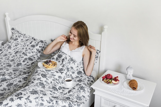 ワッフル朝食とベッドの上でコーヒーを飲んでいる女性の俯瞰