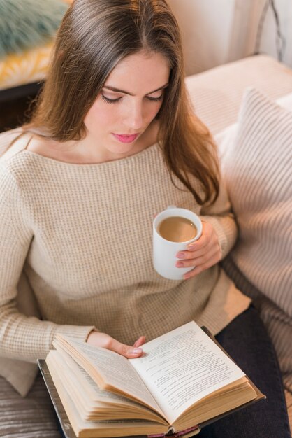 An overhead view of woman holding coffee cup reading book