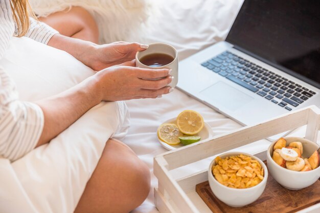 An overhead view of woman holding coffee cup sitting on bed with laptop