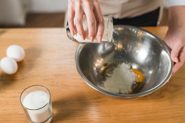 An overhead view of woman pouring flour in the utensil on the wooden table