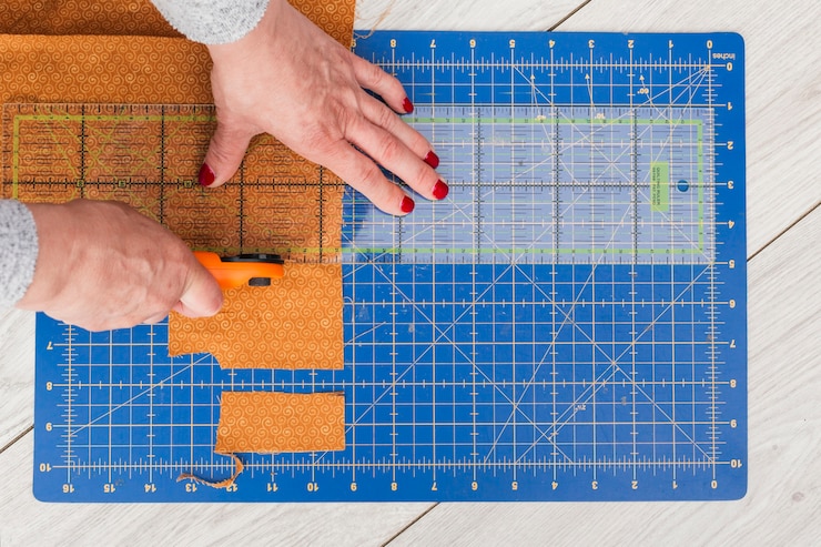 Free Photo an overhead view of a woman's hand cutting fabric to smaller part with rotary cutter on wooden table