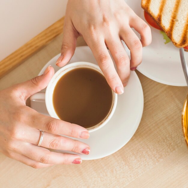 An overhead view of woman's hand holding cup of tea on wooden tray