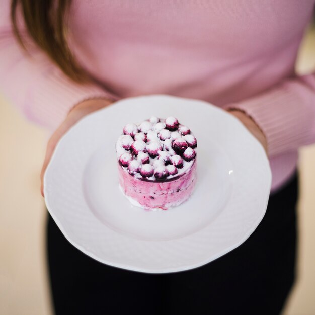 An overhead view of a woman's hand holding delicious blueberry round cake on white ceramic plate