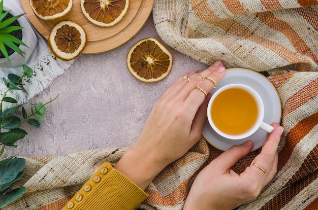 Вид сверху женская рука держит чашку травяного чая и сушеный лимон на текстурированном фоне